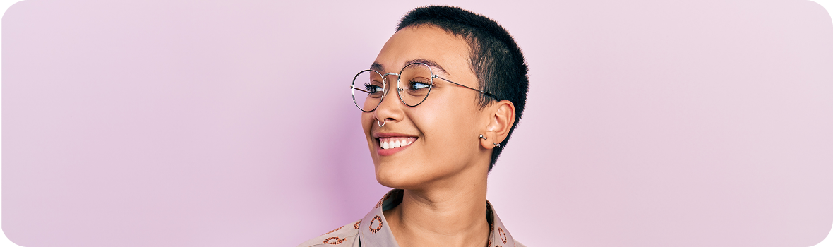 Women with short hair and round glasses smiling and looking to the side in a room with pink walls