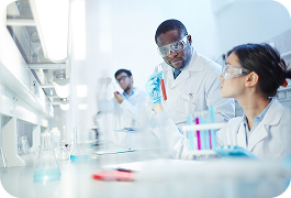 Three medical professionals wearing goggles working at a laboratory desk and holding up tube samples