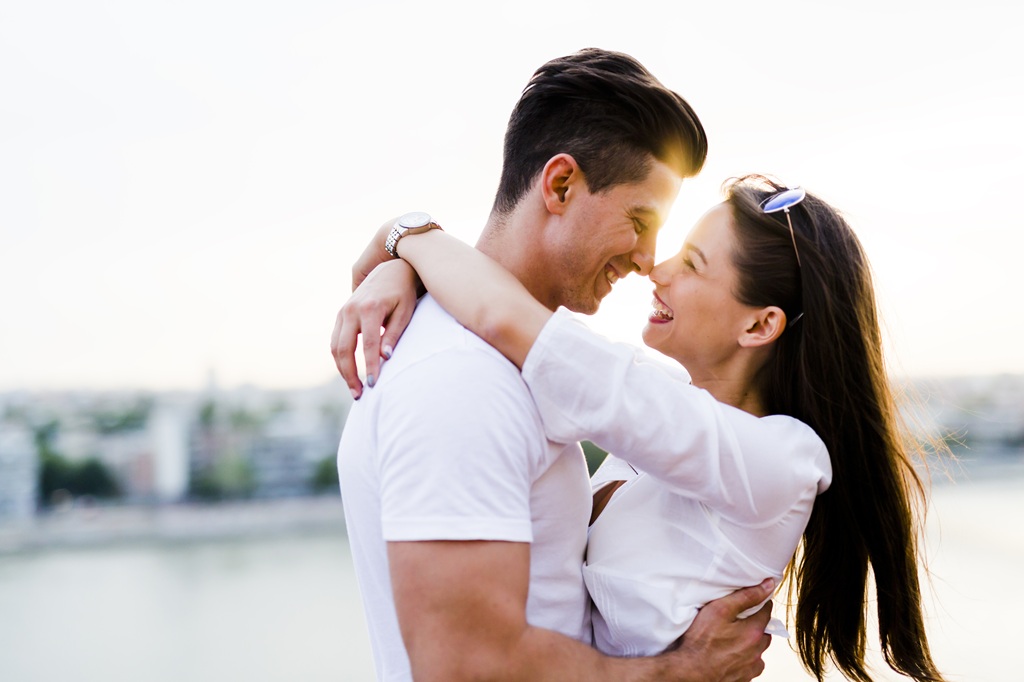 Woman with brown hair and white shirt with her arms around her boyfriend's neck as he hugs her waist